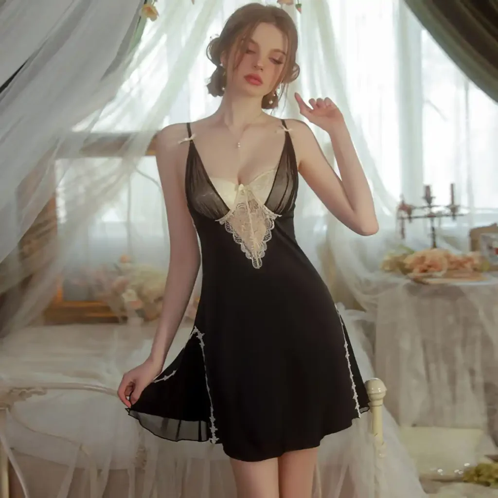 白いベッドルームでNoir Lumière Babydollを着用して立つ女性。黒シフォンのふんわりしたシルエット、胸元の白レース、裾のレースラインが分かる全身の着用イメージ。